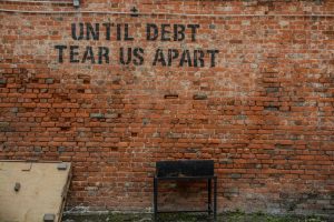 A brick wall with the words "Until debt tear us apart" painted on it.